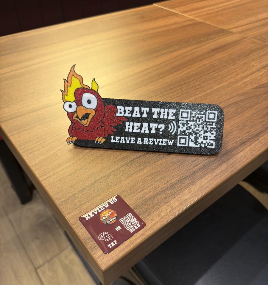 A 3D-printed table talker and a smaller table puck, both custom-branded for a restaurant, sitting on a wooden table